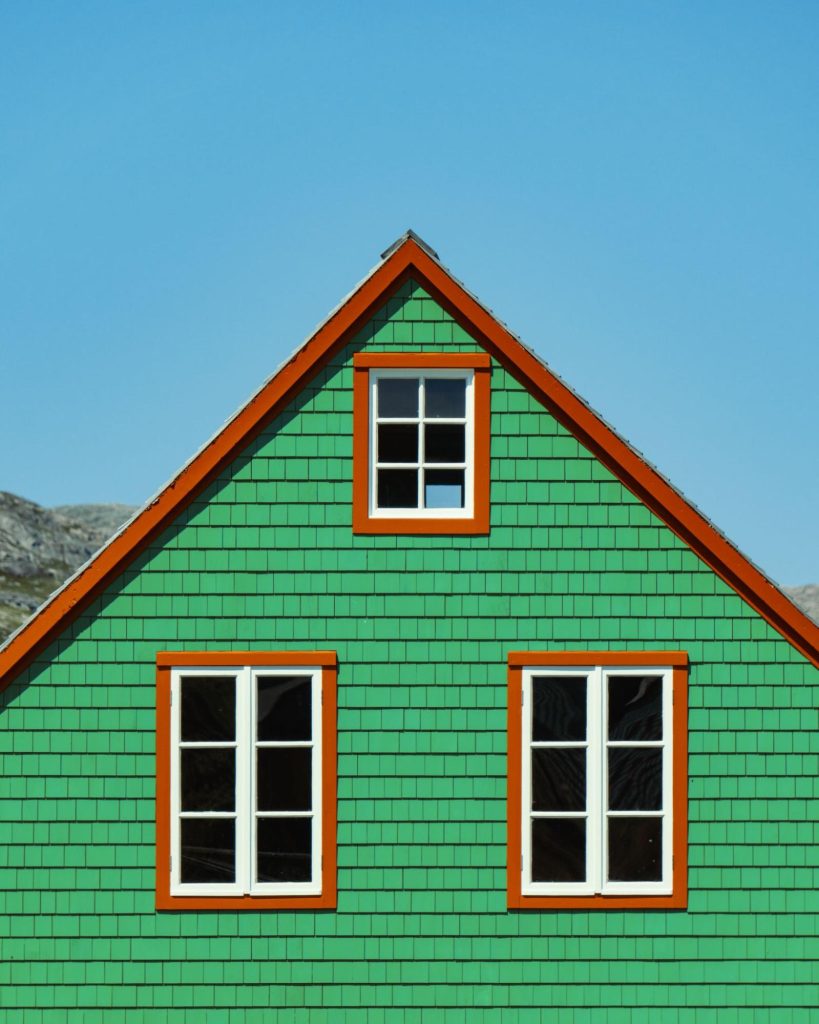 Green James Hardie siding home exterior with orange trim and three white windows against blue sky.